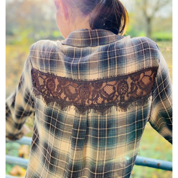 Woman wearing a plaid shirt with lace detail on the back, standing outdoors in sunlight.