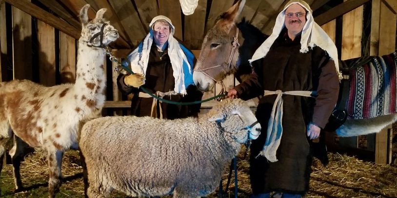 Two men in traditional attire with farm animals inside a barn.