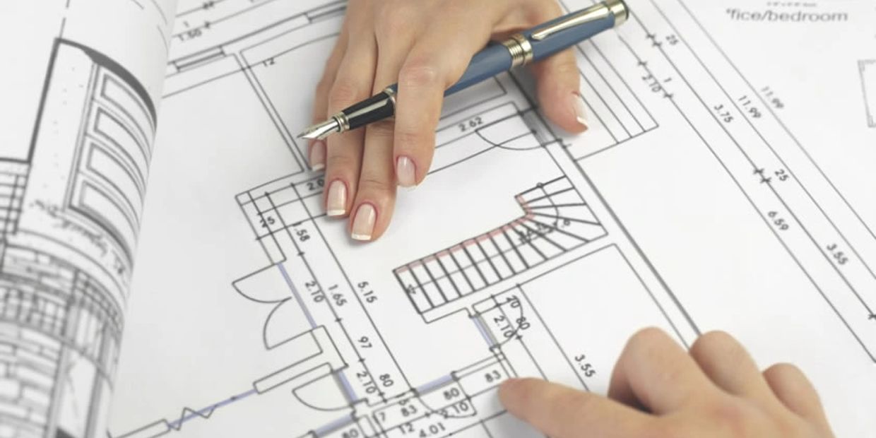 Hands pointing at architectural blueprints with a pen.