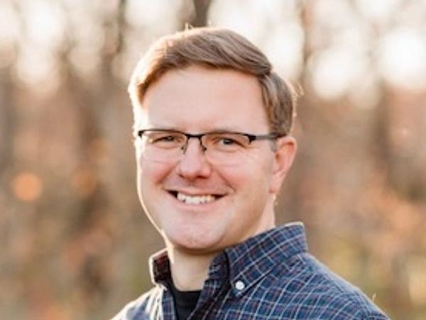 Smiling man wearing glasses and a plaid shirt outdoors.