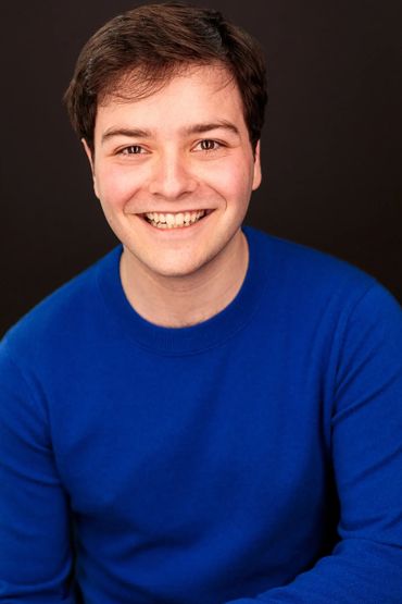Young man smiling warmly in a blue sweater against a black background.