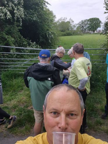 Man taking selfie with group of people outdoors near a metal gate.