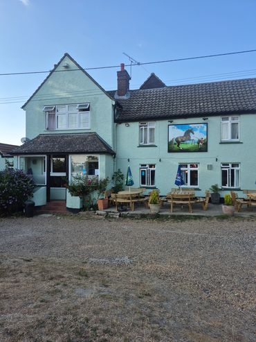 A quaint countryside pub with outdoor seating and a horse sign.