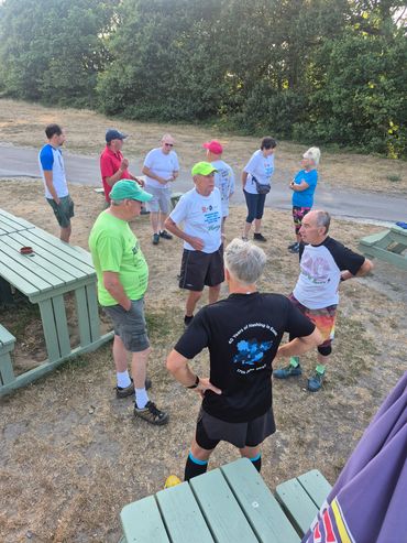 Group of people standing and talking outside near picnic tables.