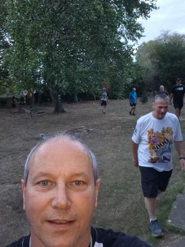 Man taking a selfie outdoors with others in the background.