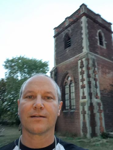 Man taking selfie near old brick tower during twilight.