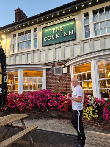 Man standing outside The Cock Inn with vibrant flowers.