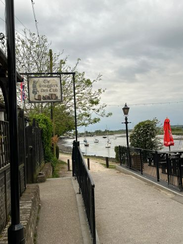 Pathway near a waterfront bar with boats and cloudy sky.
