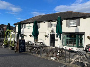 The exterior of The Astwood Bell pub with outdoor seating and umbrellas.