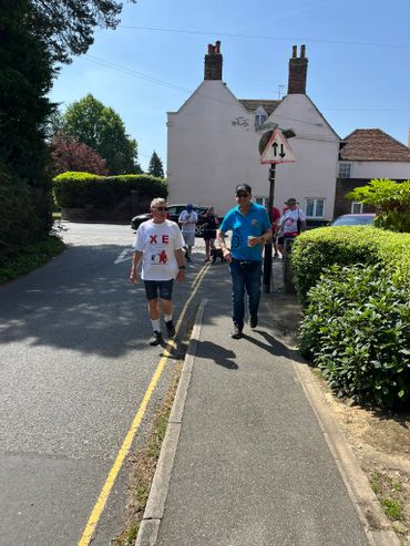 Group of people walking on a sunny street near a house with chimneys.