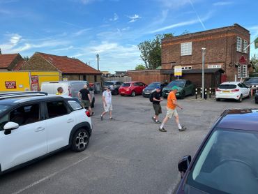 People walking in a parking lot near cars and buildings.