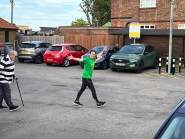 Man in green waving while walking in parking lot.