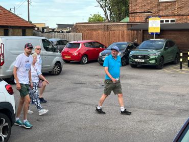 Four people walking in a parking lot near parked cars.