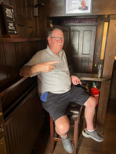 Older man relaxing on a stool in a cozy pub.