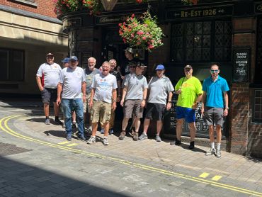 Group of men standing on the street near a building with flowers.