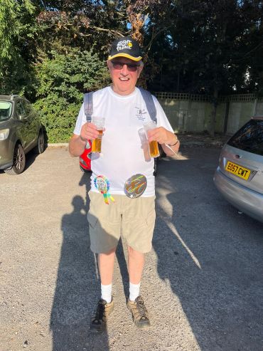 Man holding two glasses of beer outdoors on a sunny day.
