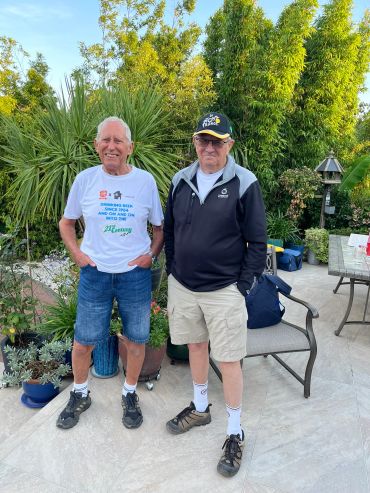 Two elderly men standing outdoors in casual attire.