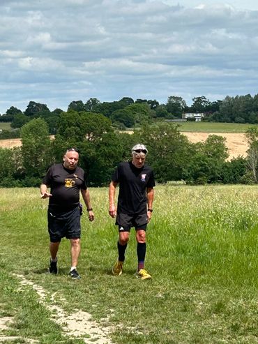 Two men walking on a grassy path in a countryside setting.