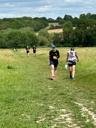 People walking and jogging on a grassy trail in a countryside setting.