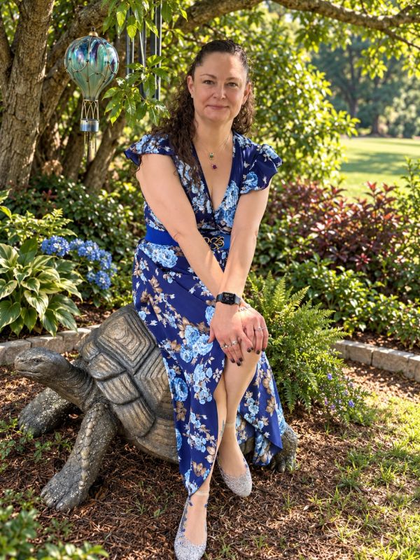 Woman in floral dress sitting on a stone tortoise statue in a garden.