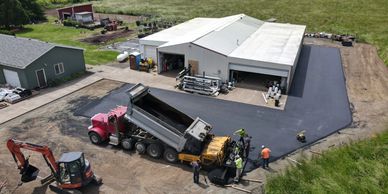 Construction workers paving a driveway around a white warehouse building.