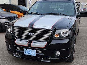 Black Ford truck with racing stripes and custom license plate.