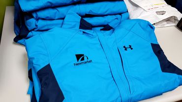 Blue jackets with Newmarket and Under Armour logos folded on a table.