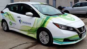 White electric Nissan car with green and blue wave decals and Vaughan branding.