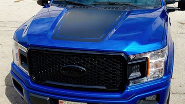 Front view of a blue Ford truck with a black grille and hood decal.
