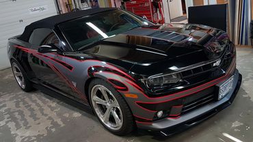 Black convertible sports car with red and gray flame decals inside a garage.