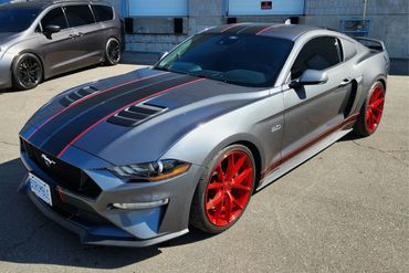 Gray Ford Mustang with black and red racing stripes and bright red rims.