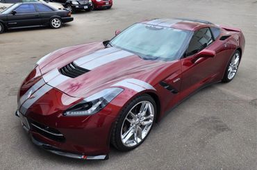 A sleek maroon Chevrolet Corvette with silver racing stripes parked outdoors.