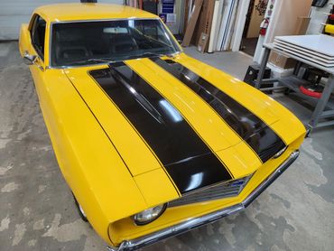 Yellow classic muscle car with black racing stripes parked indoors.