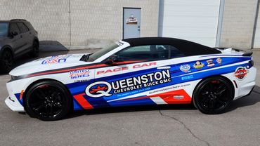 Chevrolet Camaro pace car with vibrant racing decals and sponsor logos parked outside a building.