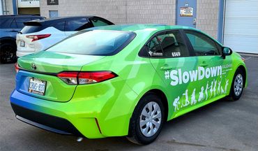 Green Toyota sedan with #SlowDown safety campaign graphics in Vaughan, Ontario.