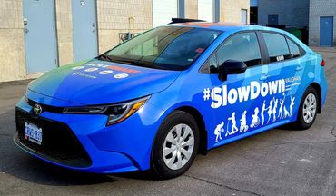 Blue Toyota car with #SlowDown safety campaign graphics.