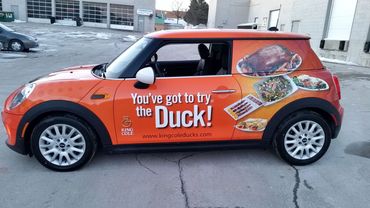 Orange Mini Cooper with a duck-themed food advertisement.