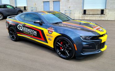 A sleek Chevrolet Camaro race car with vibrant yellow and red decals.