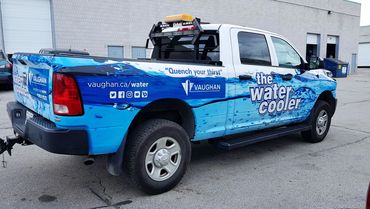 A pickup truck with a blue water-themed wrap promoting Vaughan's water services.