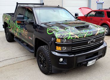 Black Chevrolet truck with green and orange tree care decals and rugged tires.