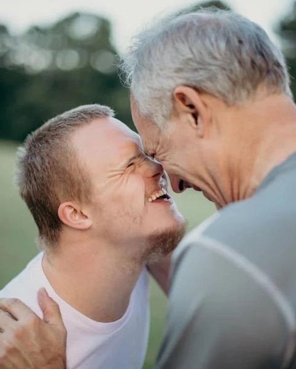 Elderly man and young man sharing a joyful moment forehead to forehead.