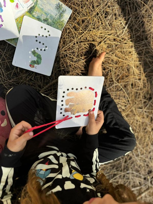 Child lacing red yarn on a bear illustration card.