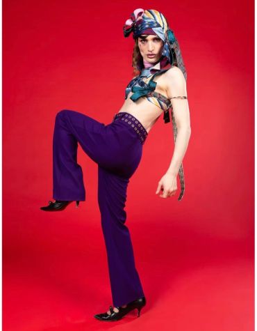Fashion model striking a bold pose in colorful attire against a red backdrop.