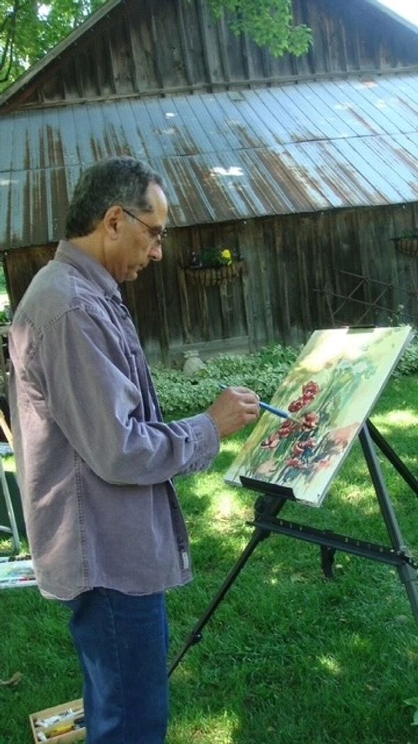 Man painting a floral scene outdoors beside a rustic wooden building.