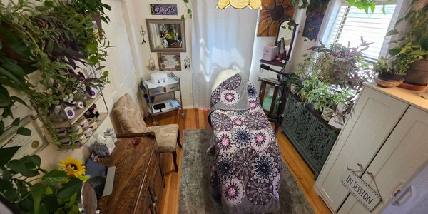 Cozy therapy room with plants, warm lighting, and a massage table.