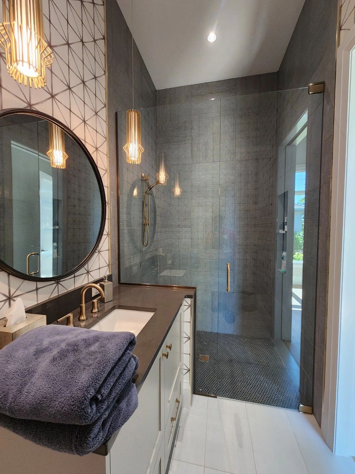 Modern bathroom with glass shower and dark gray tiles.