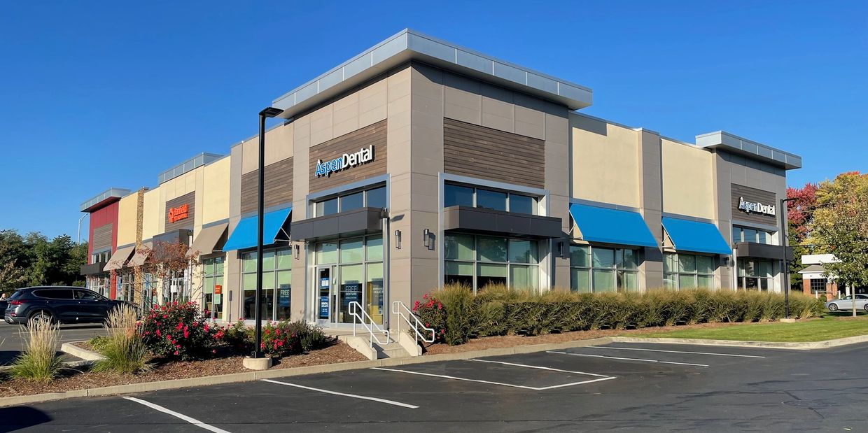 Commercial plaza featuring Aspen Dental and other businesses under a clear blue sky.