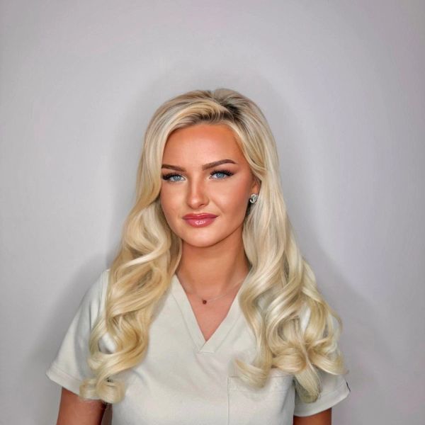 Blonde woman with styled hair posing against a plain background.