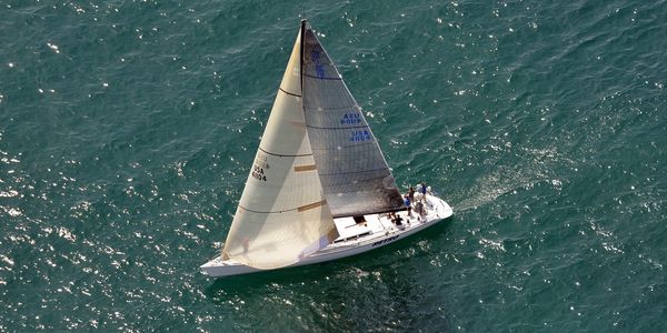 A sailboat glides through blue-green water as seen from far above.