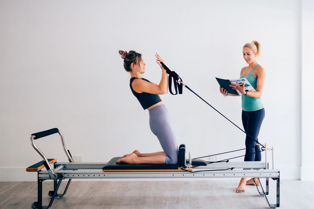 Woman exercising on a Pilates reformer machine with instructor.